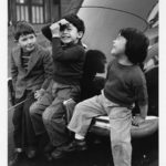Three children sit on the back of a car.